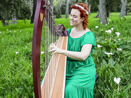 Harp player sitting outside with green bushes behind her
