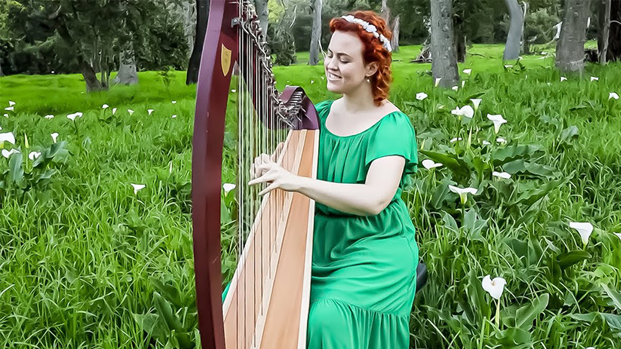 Harp player sitting outside with green bushes behind her