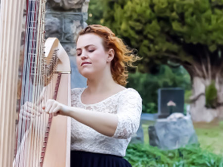 Christy-Lyn playing lever harp in garden next to stone wall