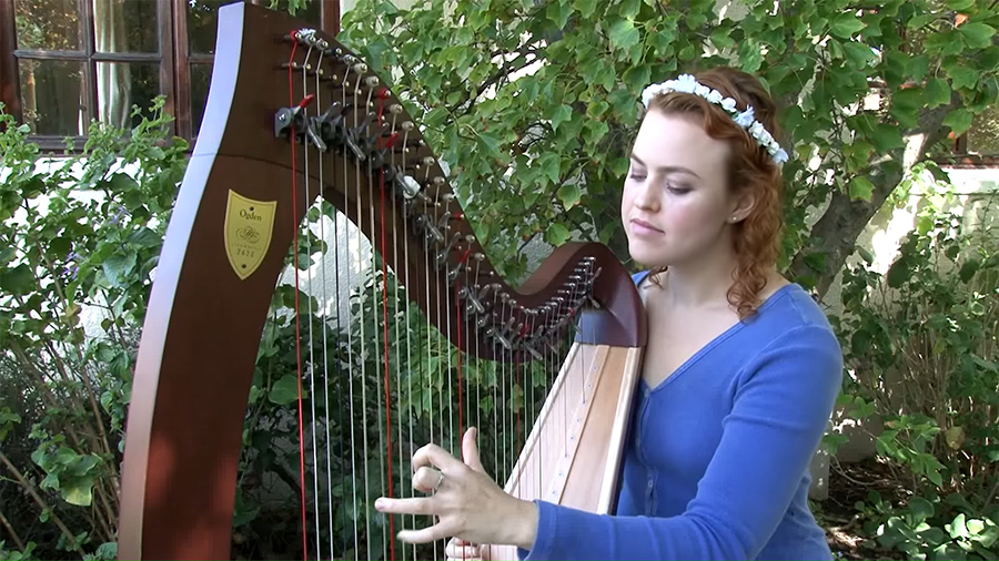Christy-Lyn playing a lever harp with green foliage in the background