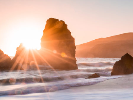 sun setting behind a rock in the ocean