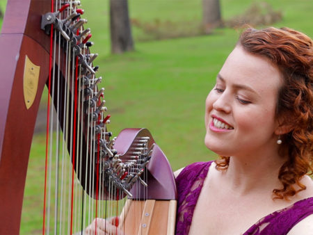 Christy-Lyn playing lever harp with green field behind her