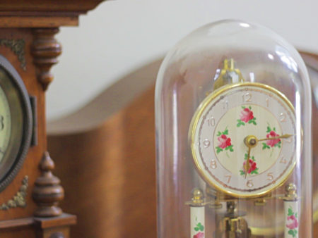 Clock under a glass cover with a grand father clock in the background