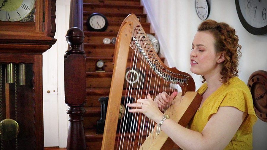 Christy-Lyn playing a lever harp surrounded by a variety of clocks