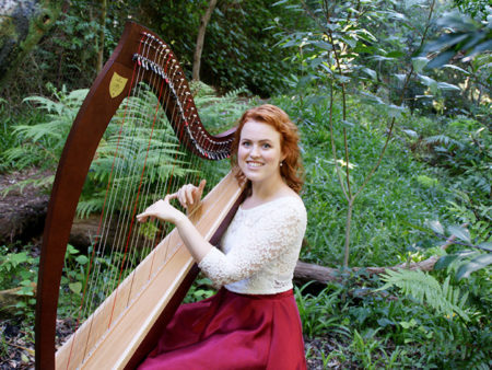 Christy-Lyn playing a harp surrounded by green foliage