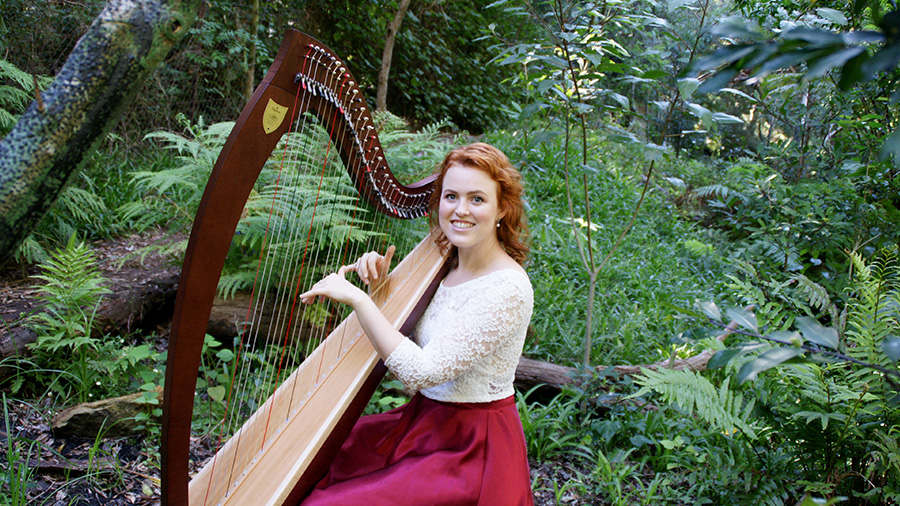 Christy-Lyn playing a harp surrounded by green foliage