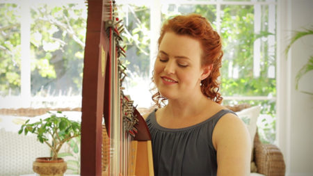 Christy-Lyn playing a harp with plants behind