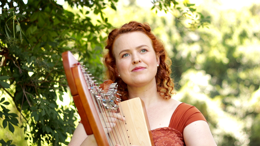 Harp player in orange dress with leafy tree behind